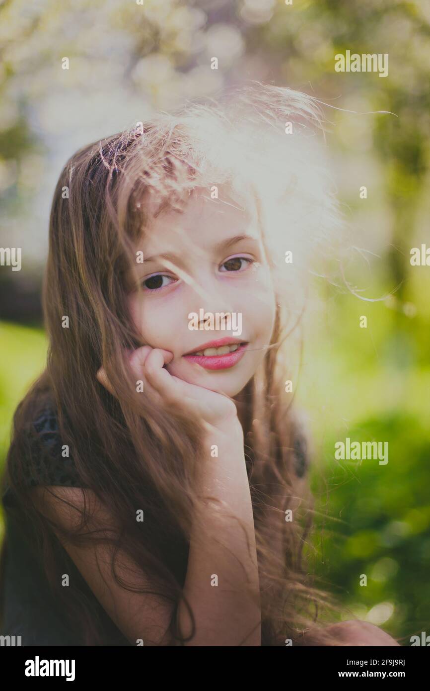 Little girl in dark dress with long hair sitting in the spring garden