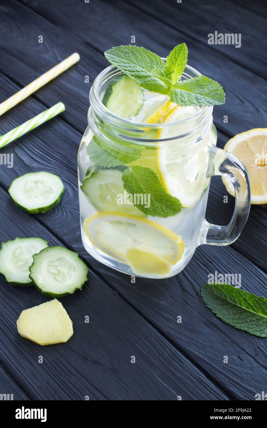 Sassy  water  slimming or infused water with lemon, cucumber and ginger in the glass on the black wooden  background. Location vertical. Stock Photo