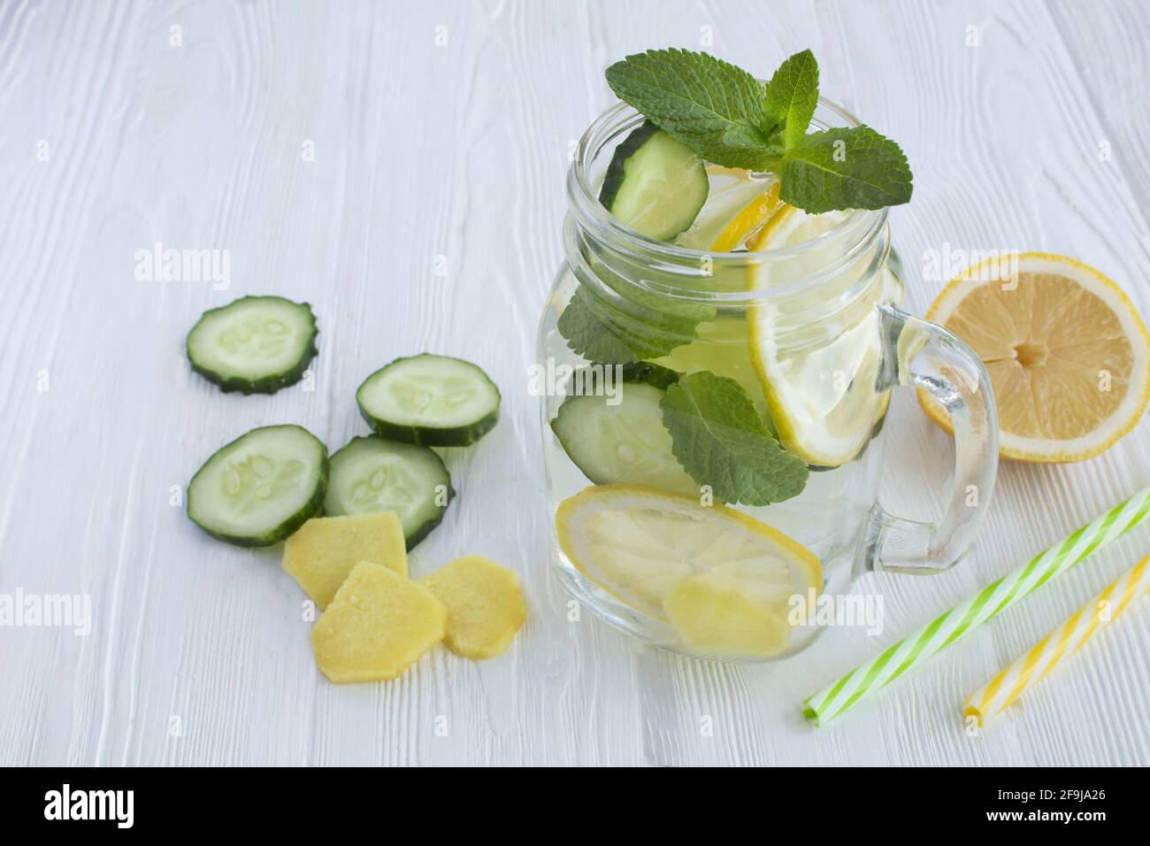 Sassy  water  slimming or infused water with lemon, cucumber and ginger in the glass on the white wooden  background. Closeup. Stock Photo