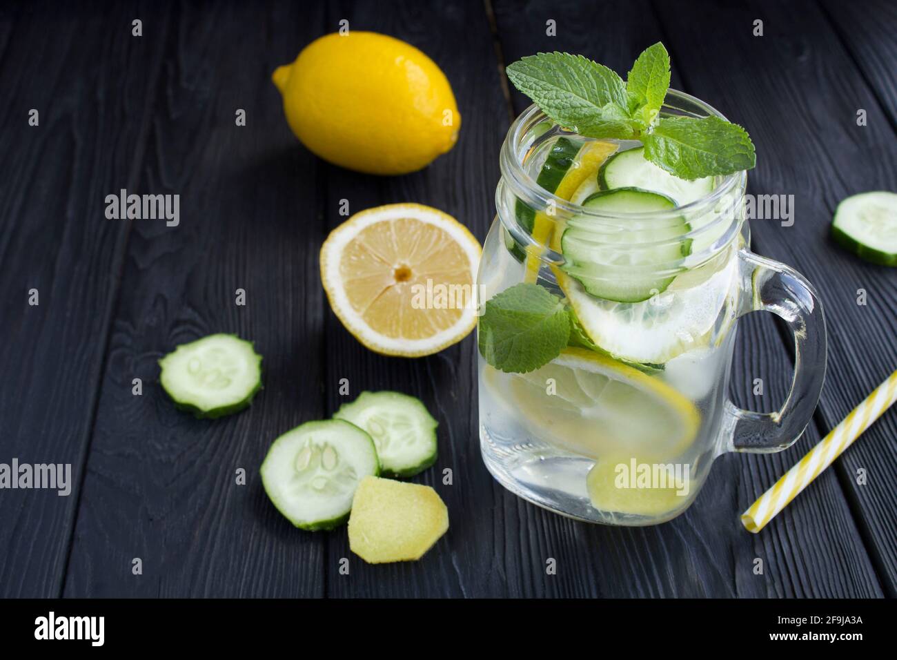 Sassy  water  slimming or infused water with lemon, cucumber and ginger in the glass on the black wooden background.  Copy space. Stock Photo