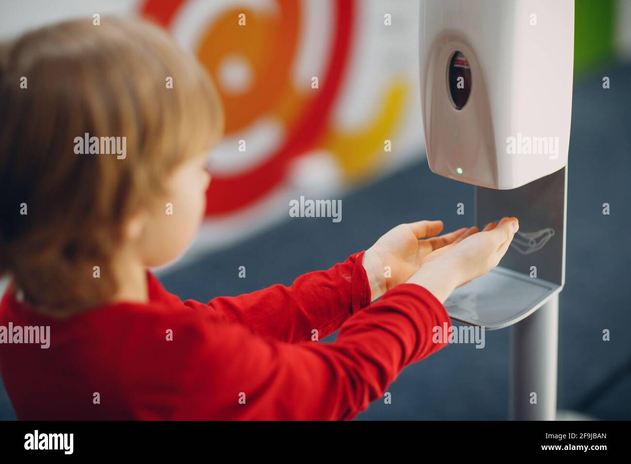 Child boy kid using automatic alcohol gel dispenser spraying on hands sanitizer machine antiseptic disinfectant, new normal life after Coronavirus COVID-19 pandemia. Stock Photo