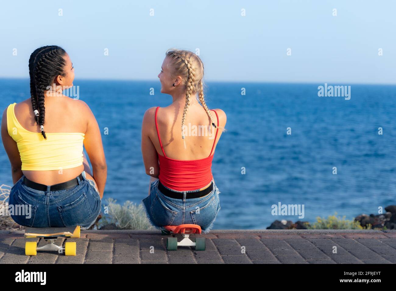 Girls sitting on skateboard and looking at each other. Outdoors, urban lifestyle.  Relax and friendship concept. Stock Photo