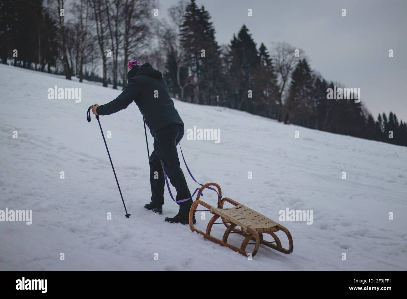 Climber pulls to the top of a wooden sled to ride on the piste.  Hardworking. Candid portrait of a man pulling a sledge, which he has hooked  behind his Stock Photo -