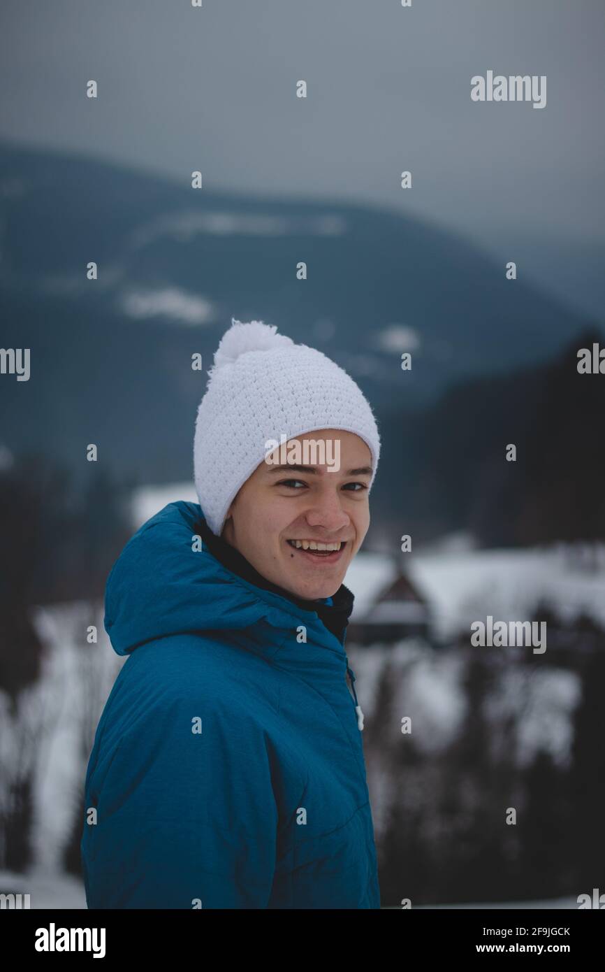 Candid portrait of a boy with a childish joyful smile in a winter white hat and blue jacket. Real portrait of a natural smiling teenager in winter mon Stock Photo