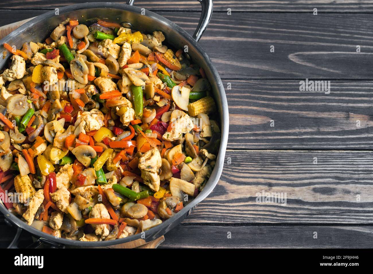 Fried chicken with a mix of vegetables in a frying pan on a wooden table top. Vegetable stew.  Stock Photo