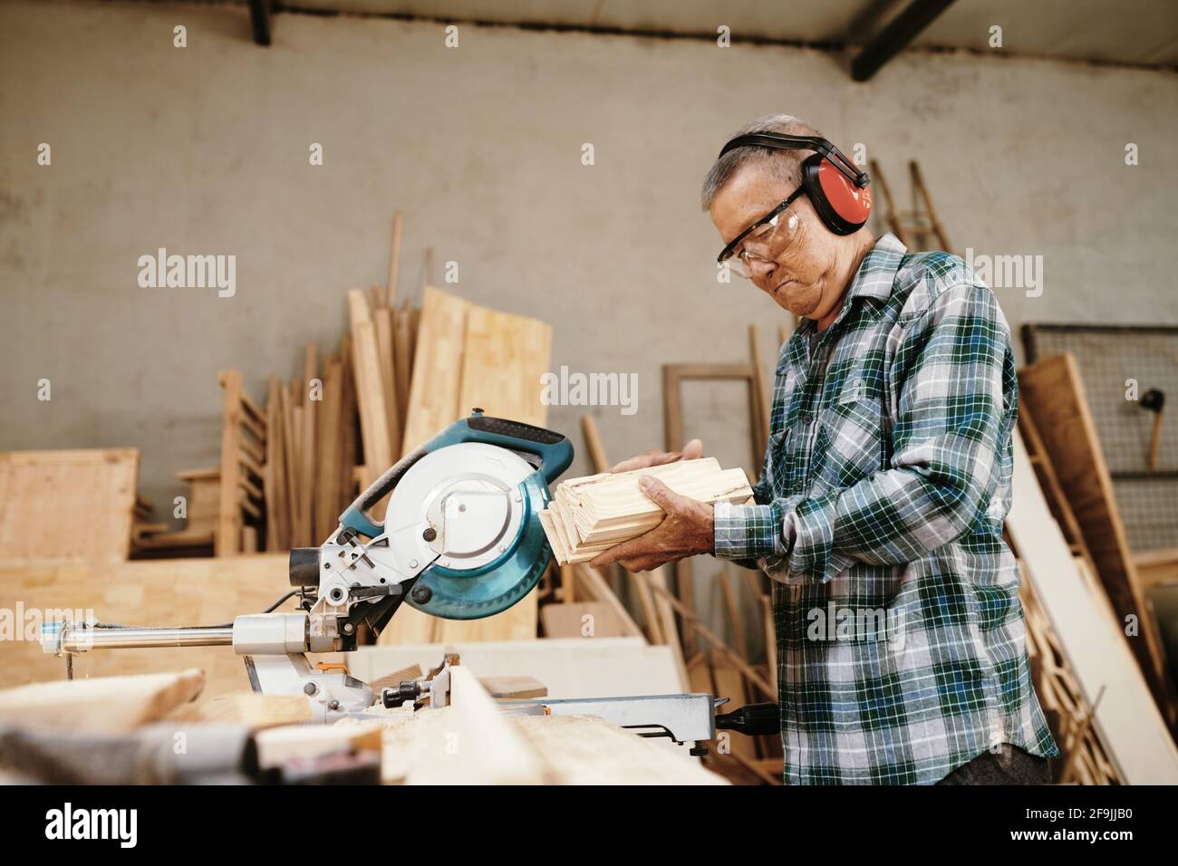 Experienced senior Vietnamese carpenter looking at wooden blocks he cut with circula saw Stock Photo