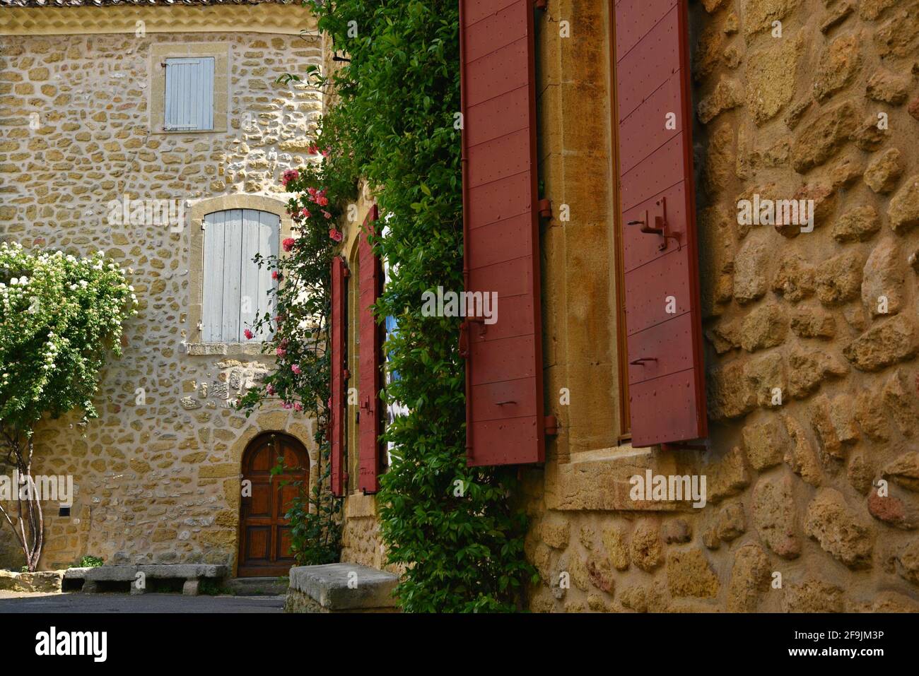 Typical Provençal style rural house stone facade with red wooden shutters in the picturesque village of Lourmarin in Vaucluse, Provence France. Stock Photo