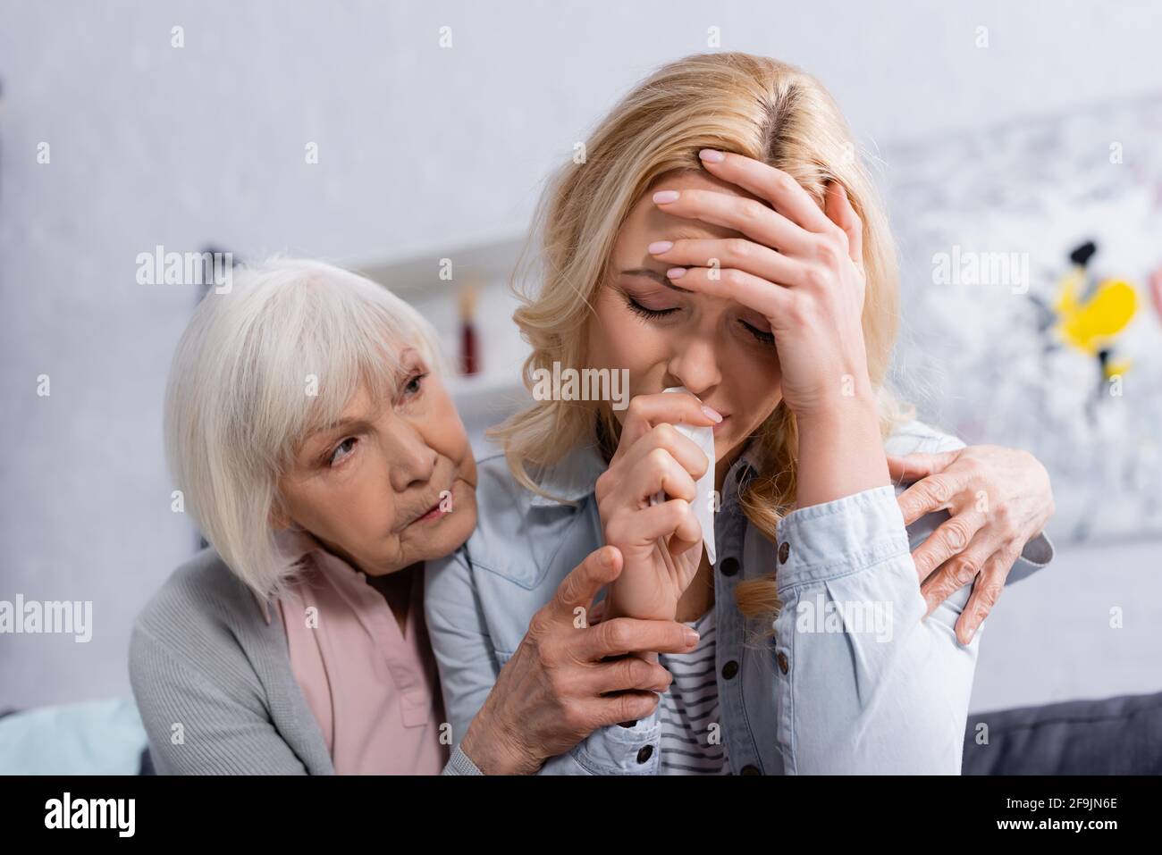 Elderly woman hugging crying daughter with napkin at home Stock Photo