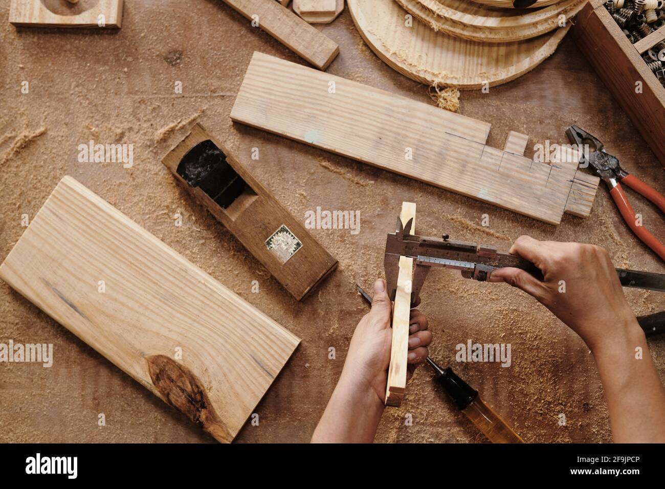 Hands of carpenter measuring wooden planks with vernier caliper, view