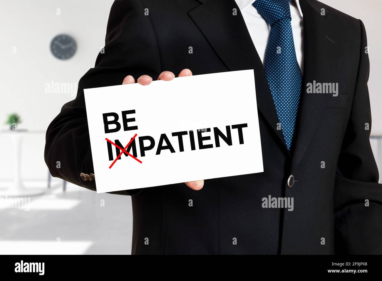 Businessman holds a card with the word be impatient transformed into be patient. Patience and persistence in business concept. Stock Photo