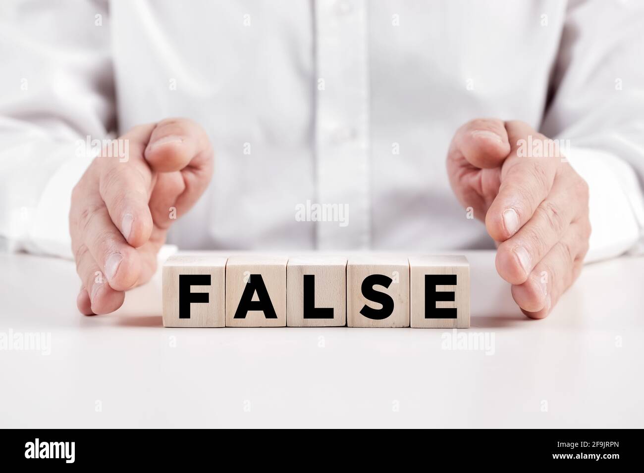 Businessman hands covers the wooden cubes with the word false. Misleading information concept. Stock Photo