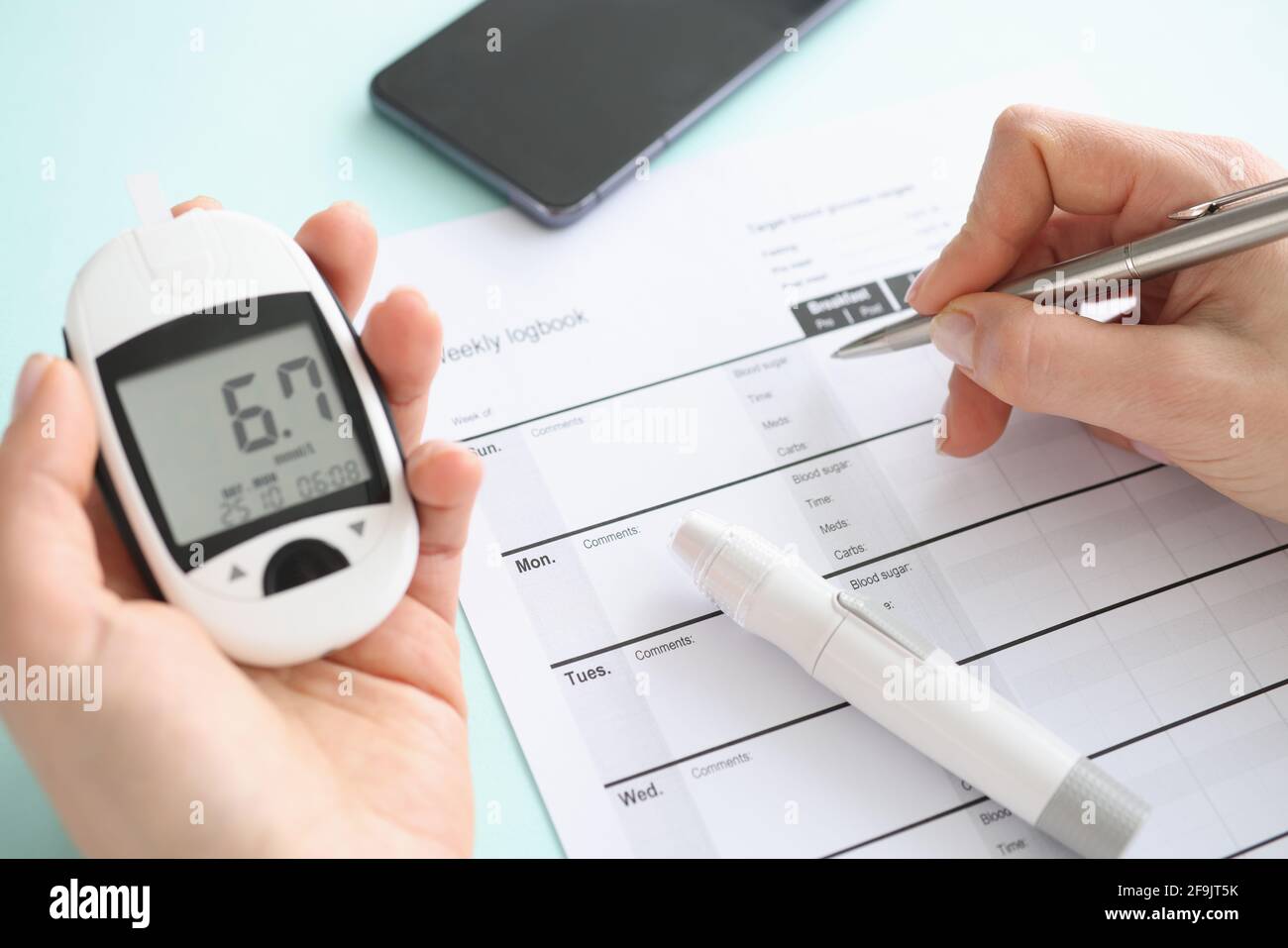 Patient holding glucometer and recording data in diary closeup Stock Photo