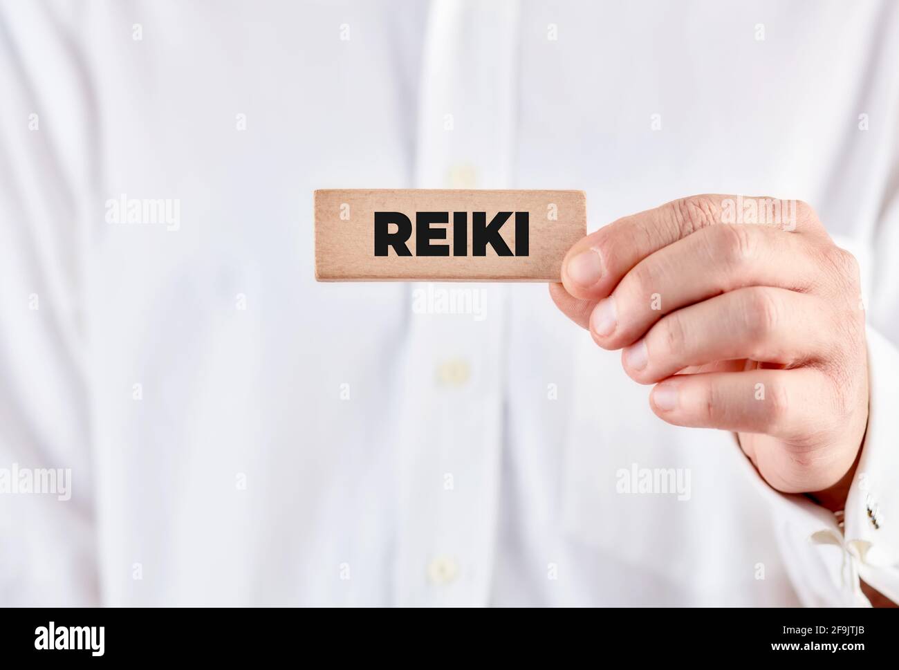 Male hand holds a wooden block with the word reiki. Stock Photo