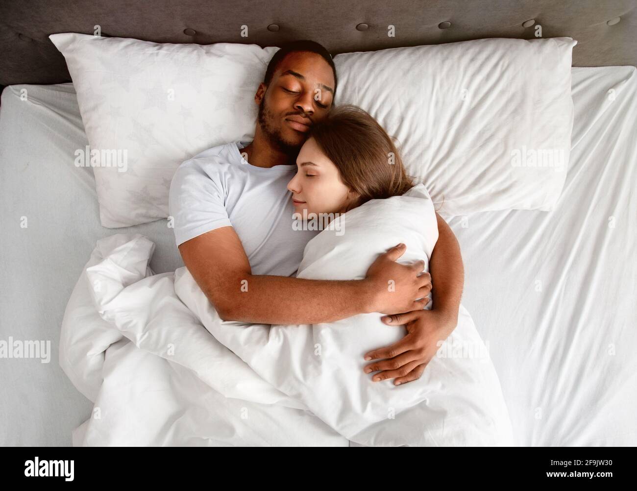 Top view of affectionate multiracial couple hugging each other while  sleeping in bed Stock Photo - Alamy