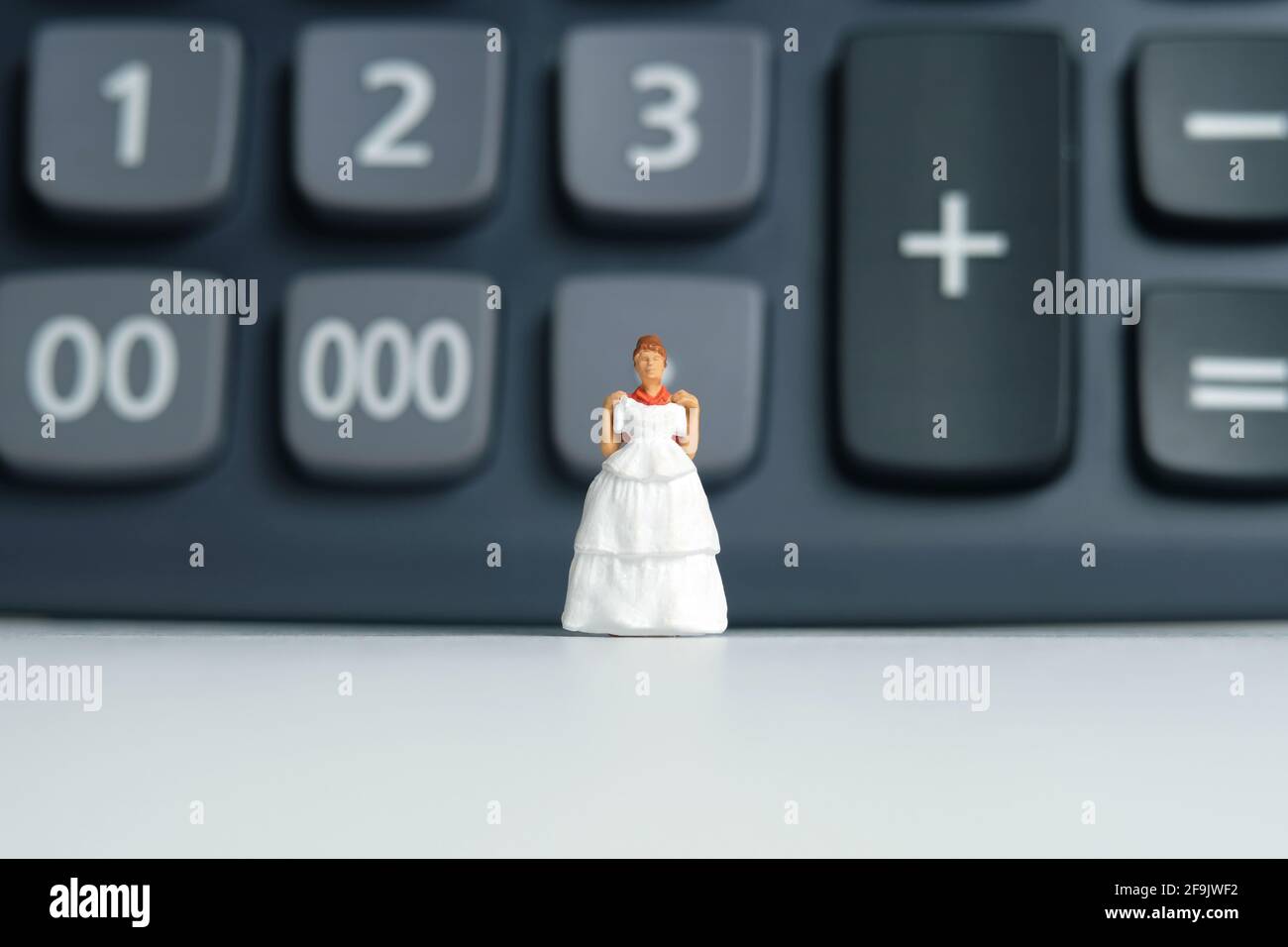 Wedding dress budget for bride, miniature people illustration concept. Woman standing above calculator. Image photo Stock Photo