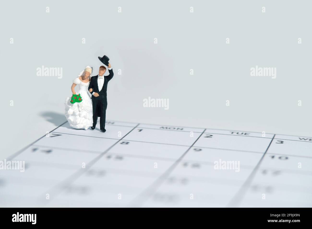 Wedding marriage day, schedule date celebration concept miniature people toy photography. Bride and groom standing above calendar. Image photo Stock Photo