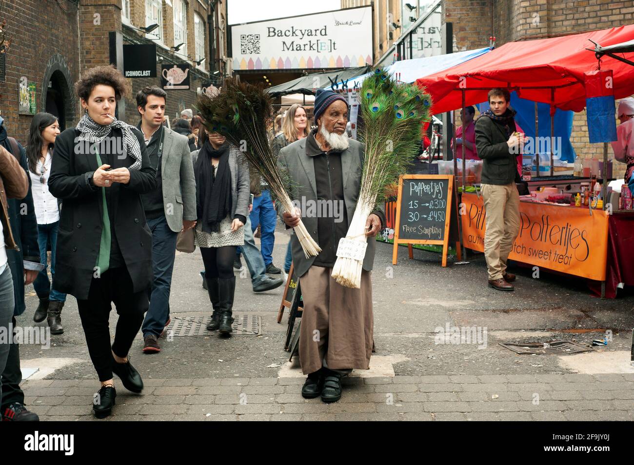 Muslim man selling peacock feathers. Sunday street market on Brick Lane, East London, UK. Apr 2014 Stock Photo