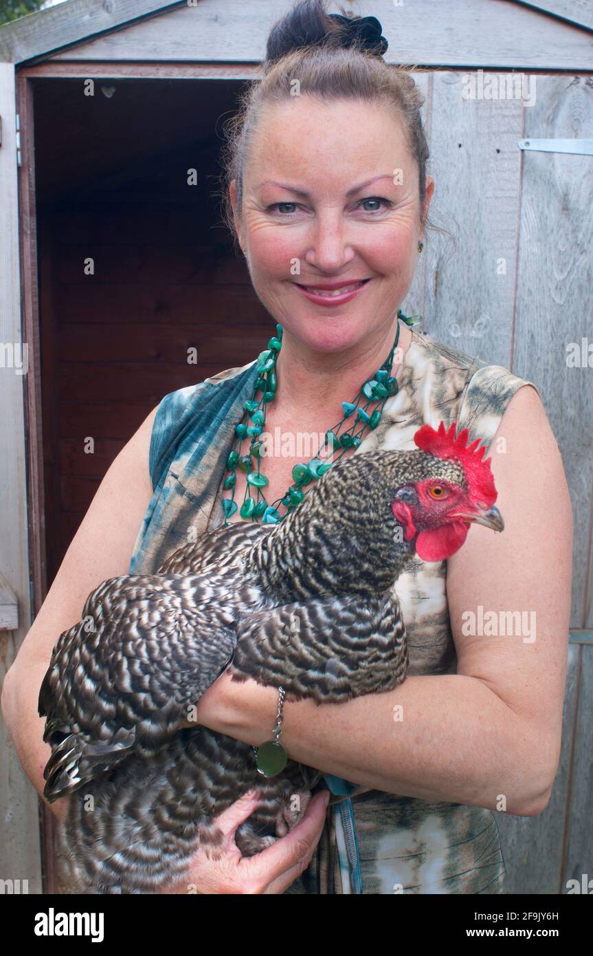 Mature female holding a speckled hen in front of a garden shed - John Gollop Stock Photo