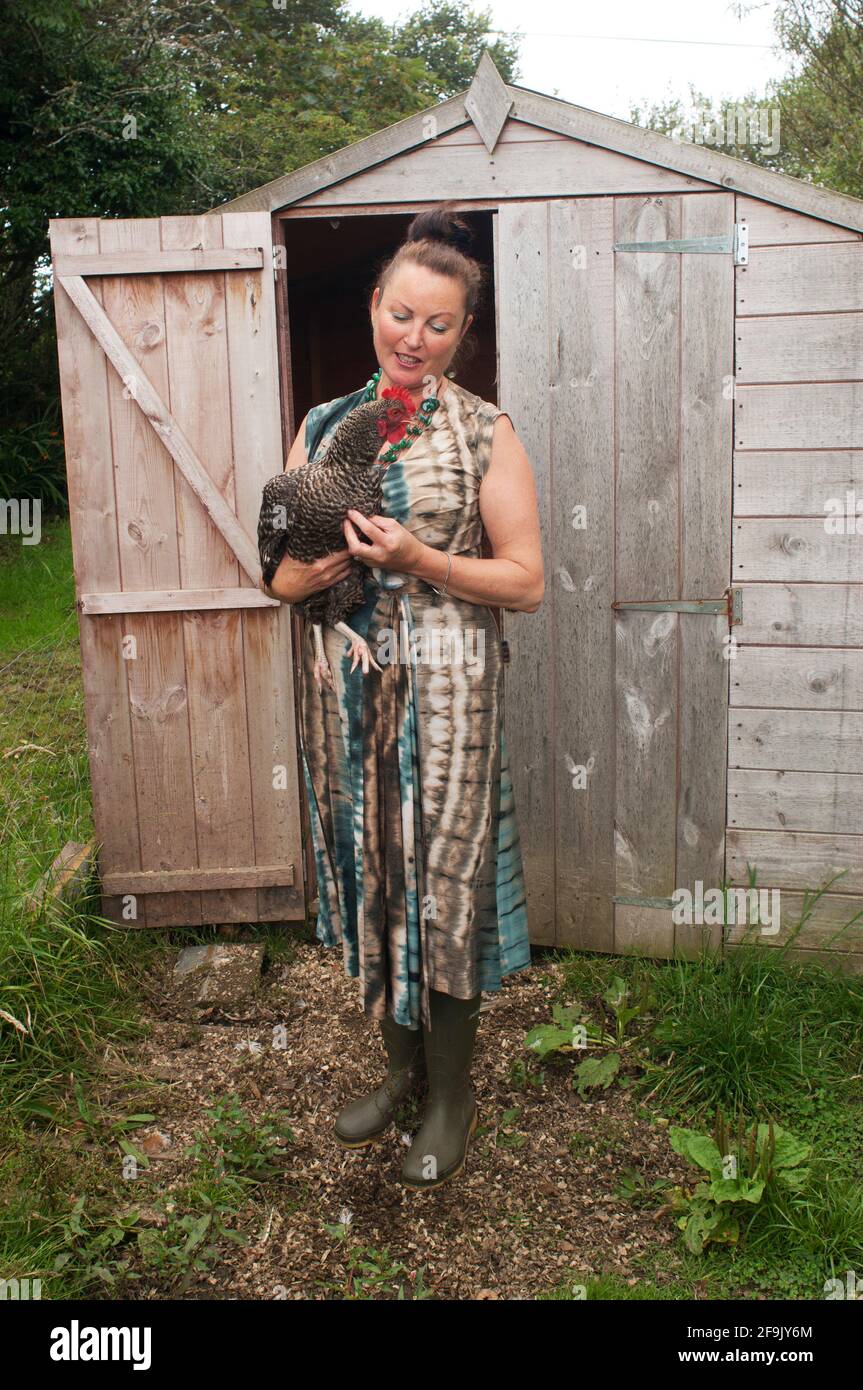 Mature female holding a speckled hen in front of a garden shed - John Gollop Stock Photo