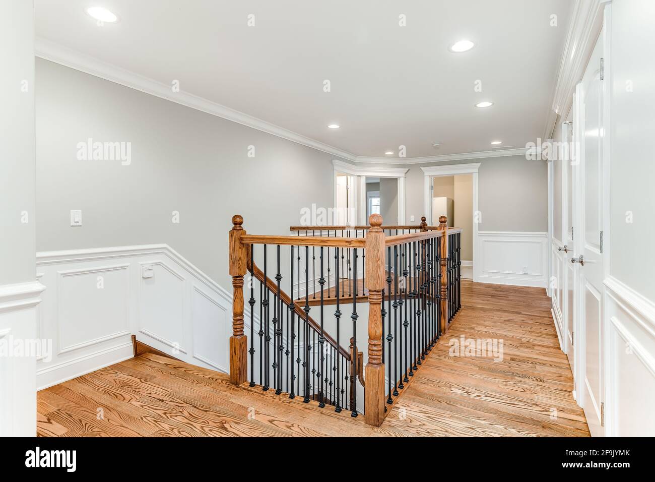 A renovated staircase with wrought iron spindles and wooden railing. The walls have a white board and batten finish around the room. Stock Photo