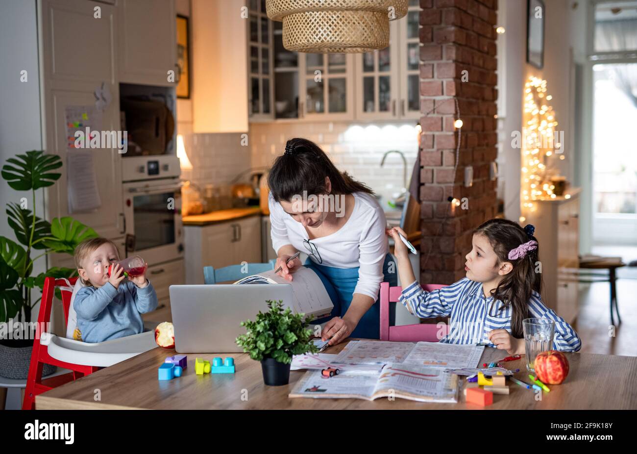 Mother with small daughter in kitchen, home schooling, office and distance learning concept. Stock Photo