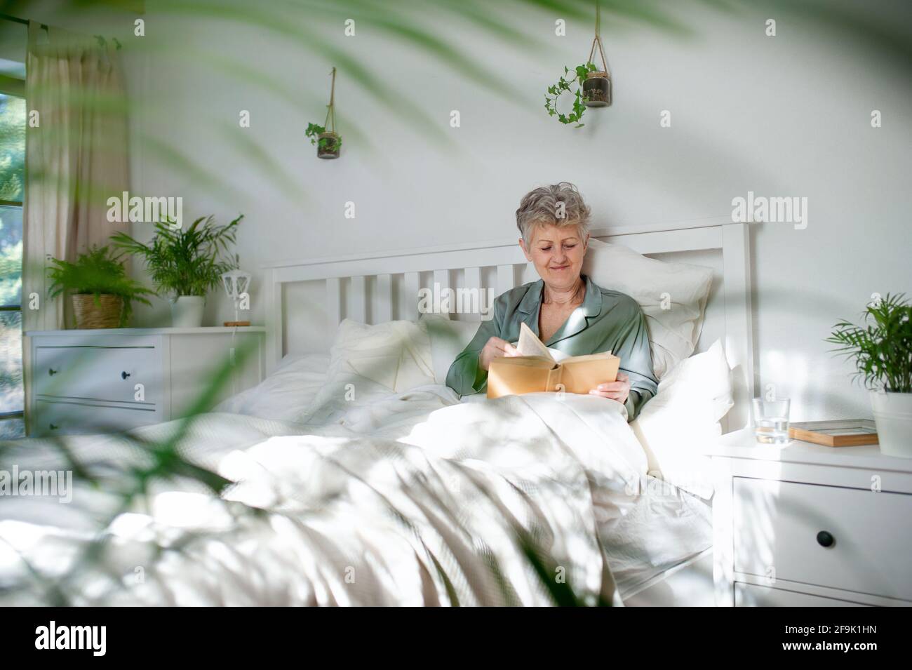 Happy senior woman reading book in bed at home. Stock Photo