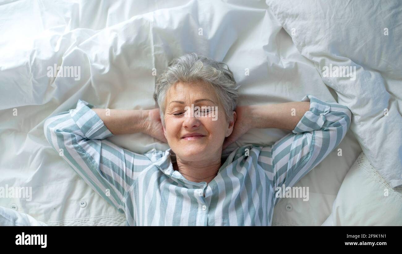 Top view of happy senior woman in bed at home, eyes closed. Stock Photo