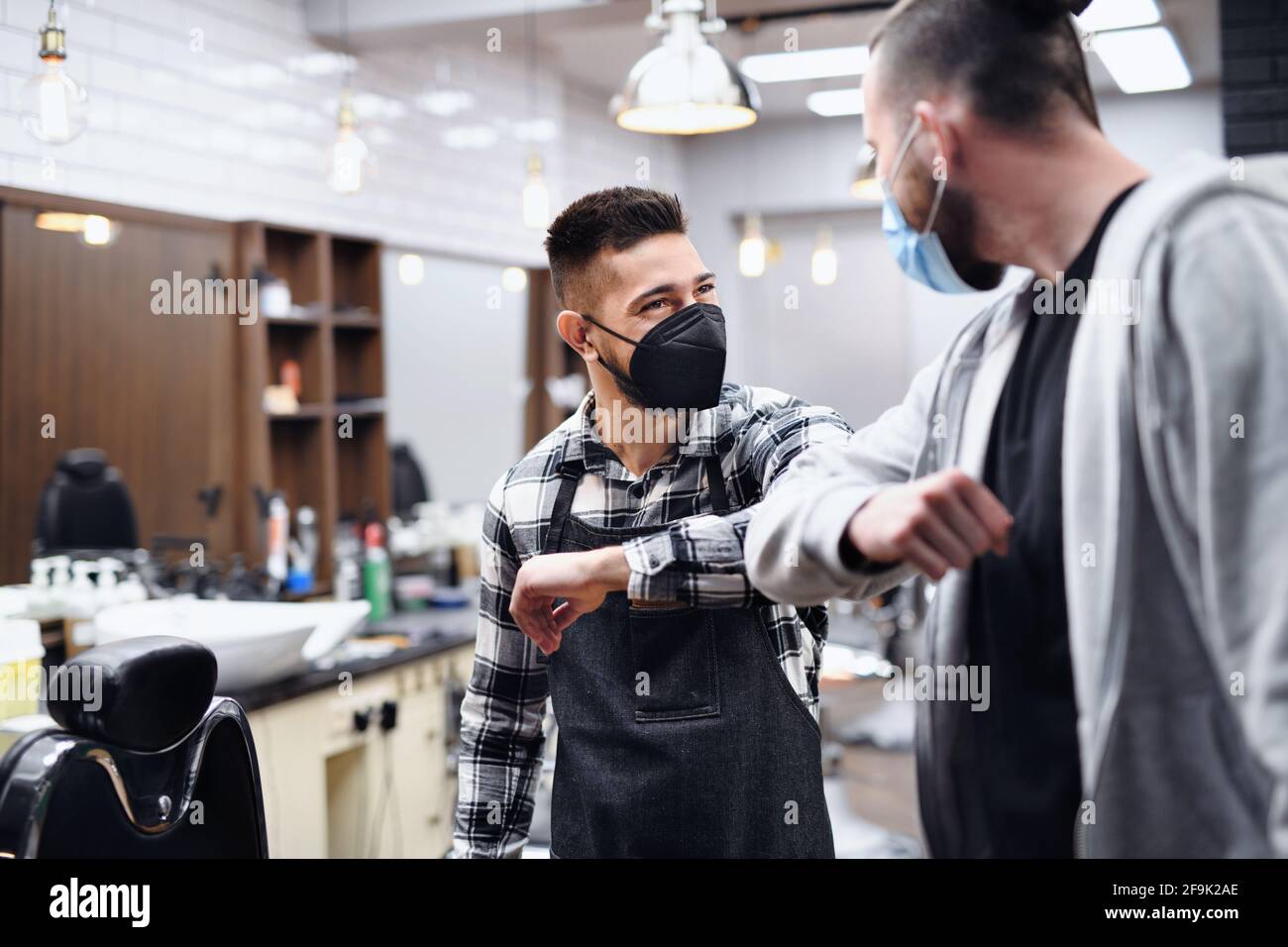 Man greeting haidresser with elbow bump in barber shop, coronavirus and new normal concept. Stock Photo