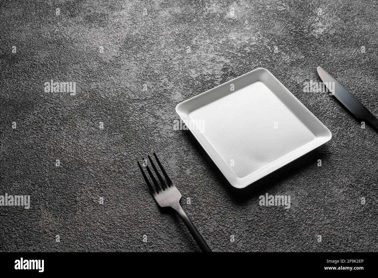 a white square empty plate, a black fork and knife. Stylish dinnerware for desserts. table setting. Suitable for interior decoration and design. copy Stock Photo