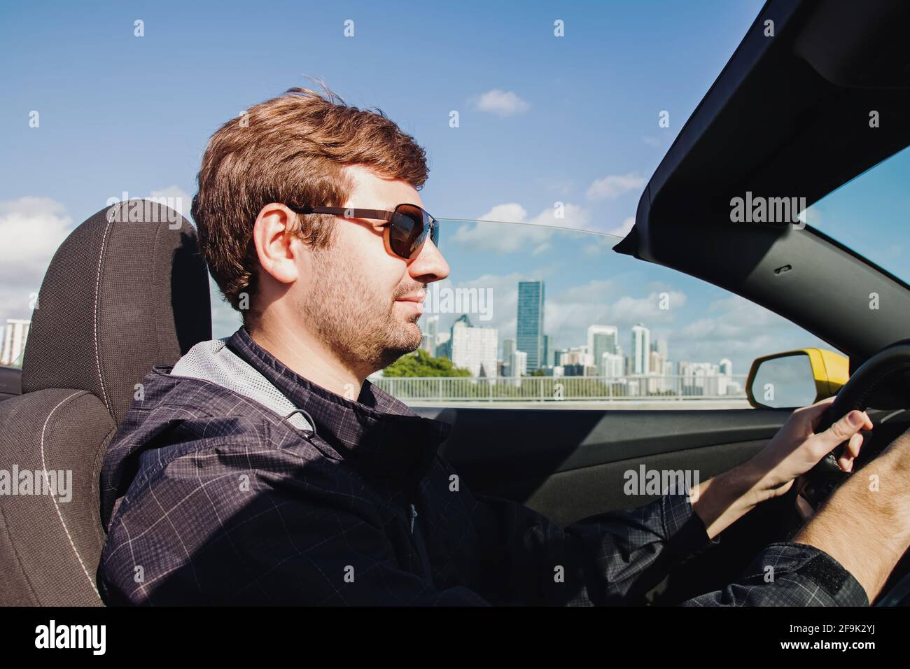 Man driving cabriolet car with a city skyline on the background Stock Photo
