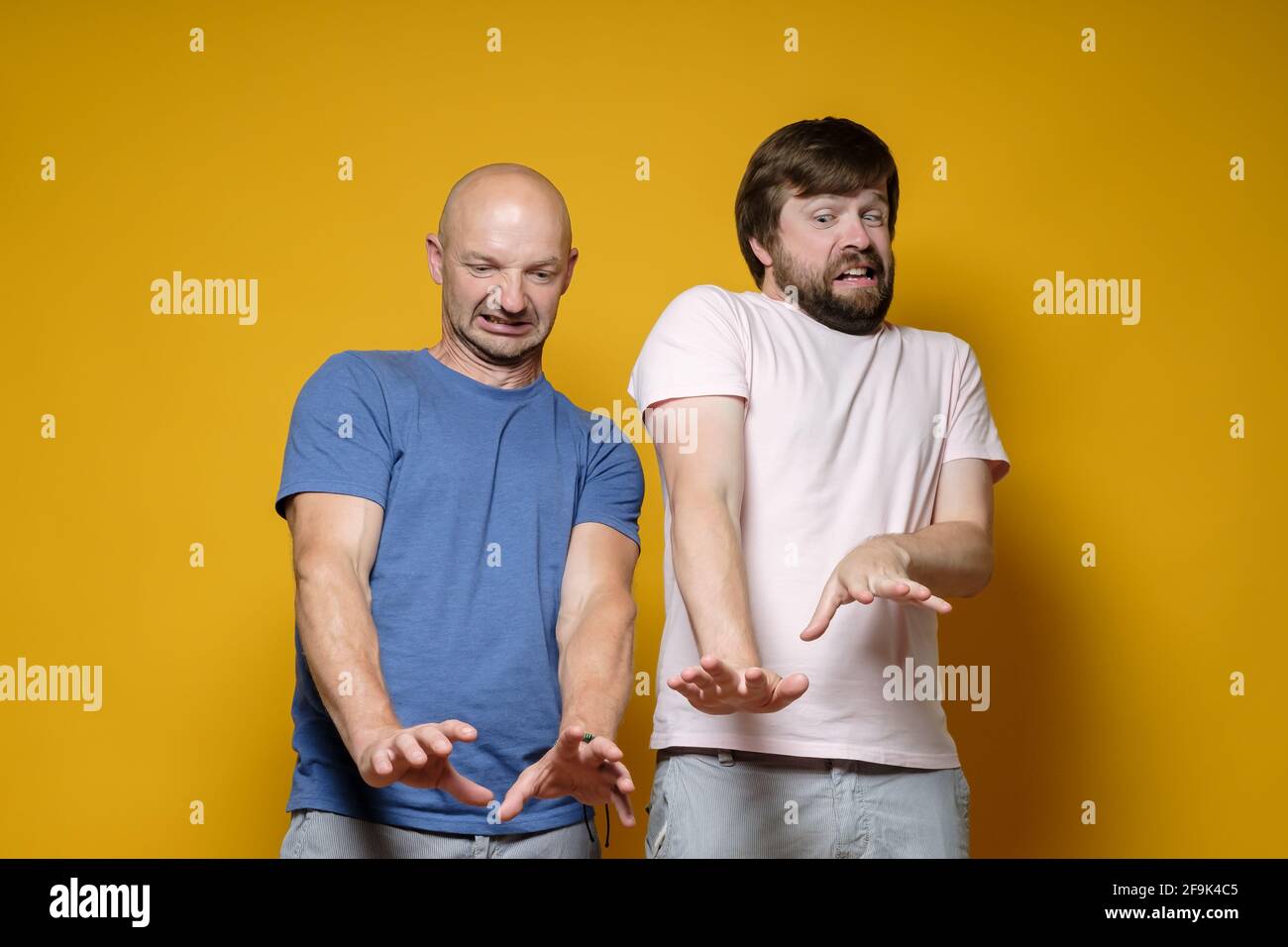 Two frightened, surprised men make a stop gesture with their arms outstretched and look down with disgust and dislike.  Stock Photo