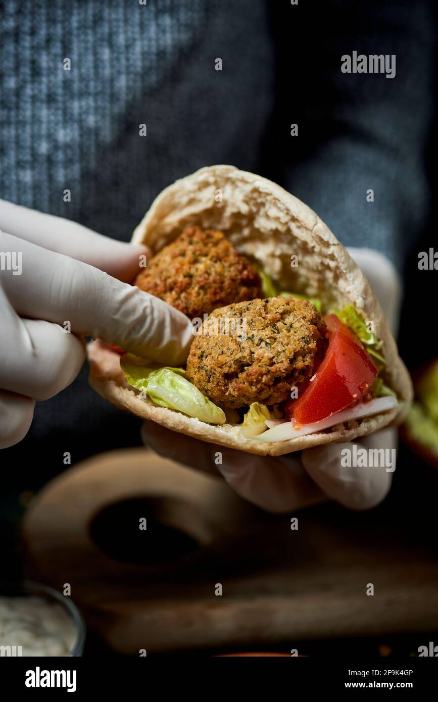 closeup of a young man, wearing latex gloves, filling a pita bread with some falafel and chopped lettuce, onion and tomato Stock Photo