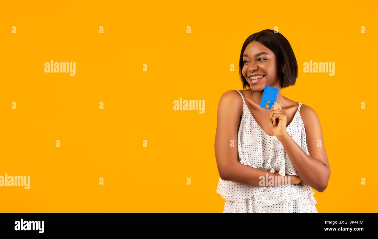 Happy black lady with credit card posing on orange studio background ...