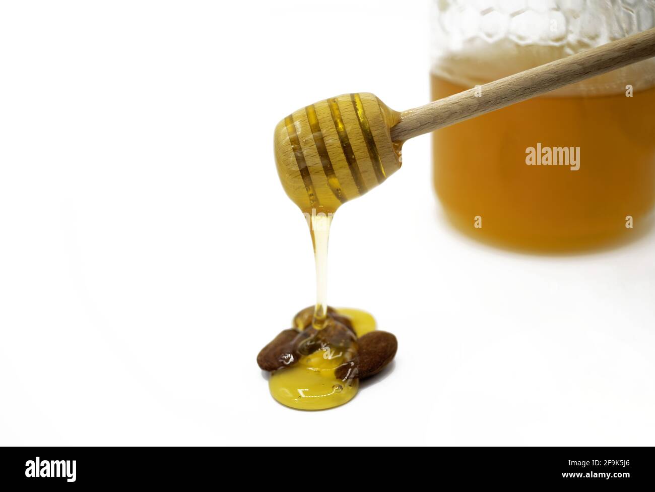 Putting with a wooden dispenser honey on some almonds. On the white background the container with honey is out of focus Stock Photo