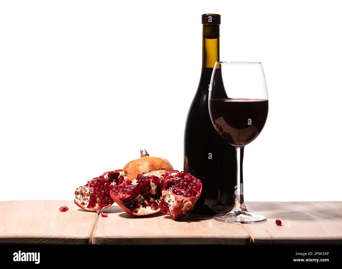 Isolated burgundy red wine bottle, wine glass and juicy pomegranate on