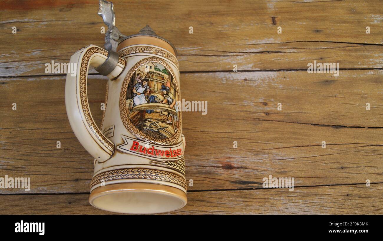 Ceramic beer mug with metal lid with high relief inscription Budweiser showing workers making beer keg in ancient time on zoomed wooden background Stock Photo