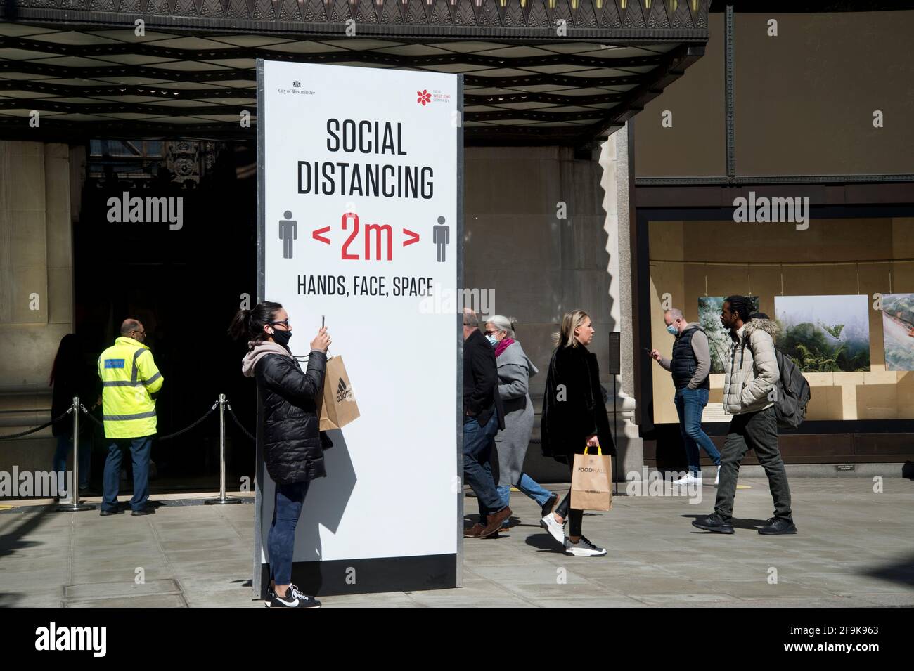 London, England, UK. Oxford Street, Selfridges, re-opened after lockdown 3. Sign reminding people to social distance and a woman taking a selfie. Stock Photo