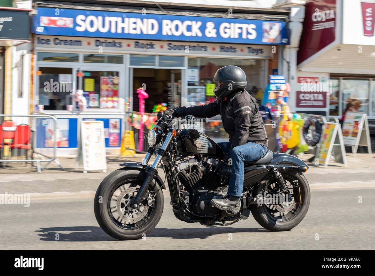 Harley Davidson Forty Eight motorcycle, motorcyclist riding in Southend on Sea, Essex, UK, on a sunny, bright Spring day. Passing Southend Rock shop Stock Photo