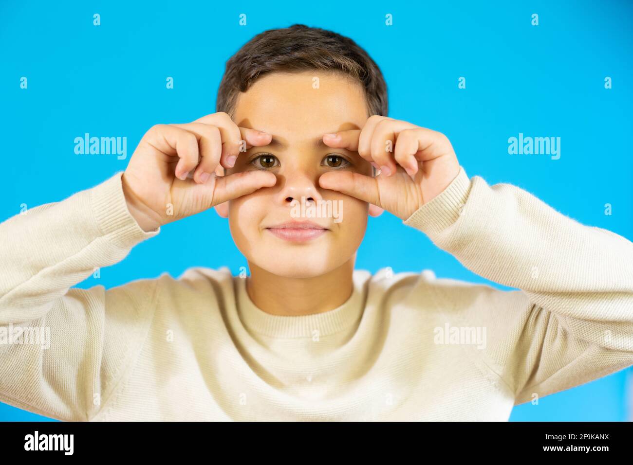 Young boy showing his eyes with hands isolated over blue background ...