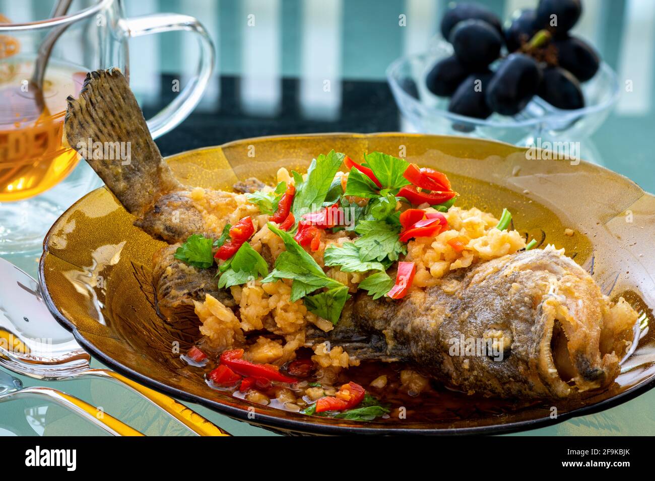 Fried grouper fish on a brown glass plate topped with condiments, Chinese cooking in Malaysia Stock Photo