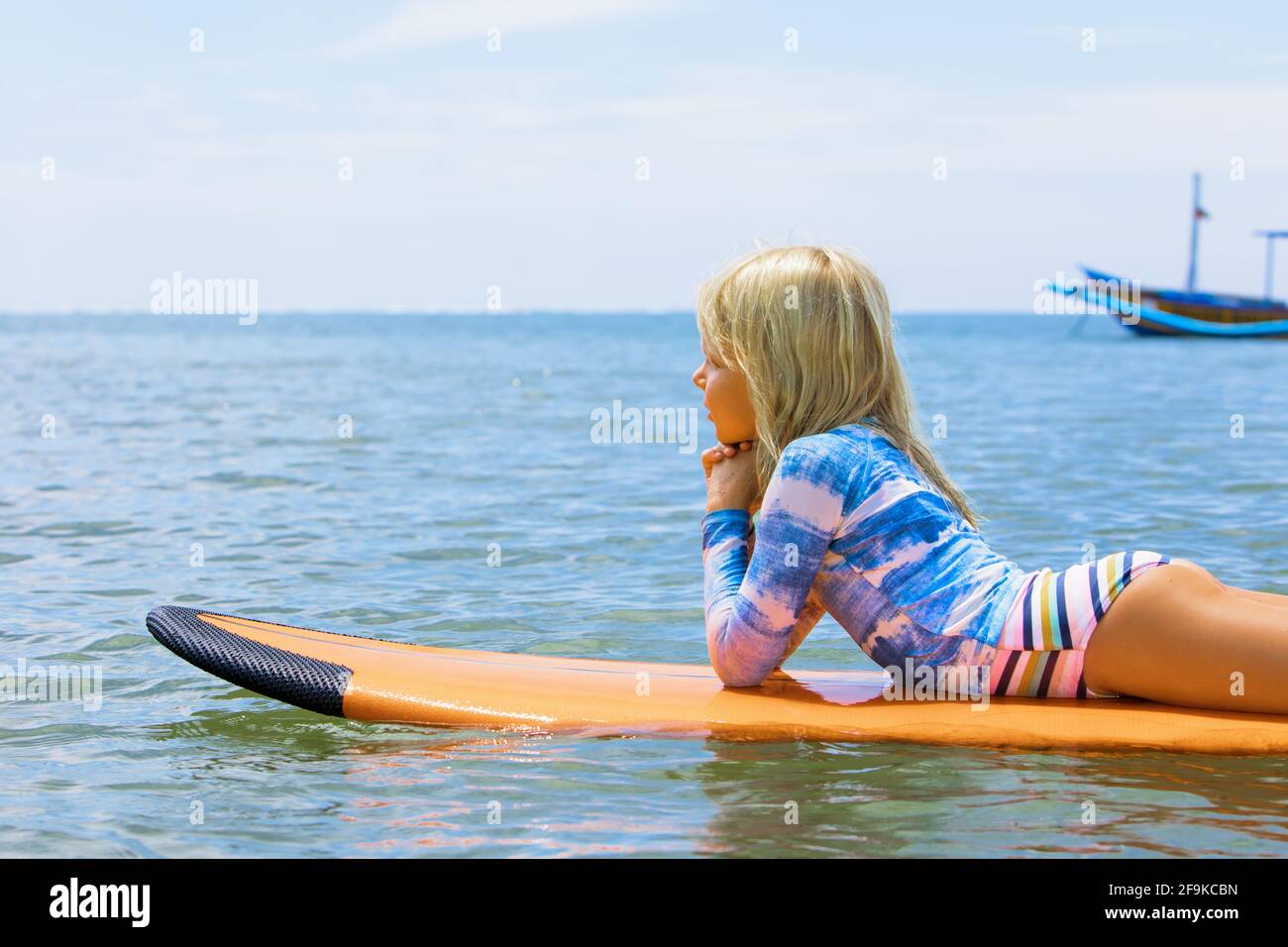 Happy girl relaxing before surfing. Surfer lying on surf board. People in water sport adventure camp, extreme activity on family summer holidays Stock Photo