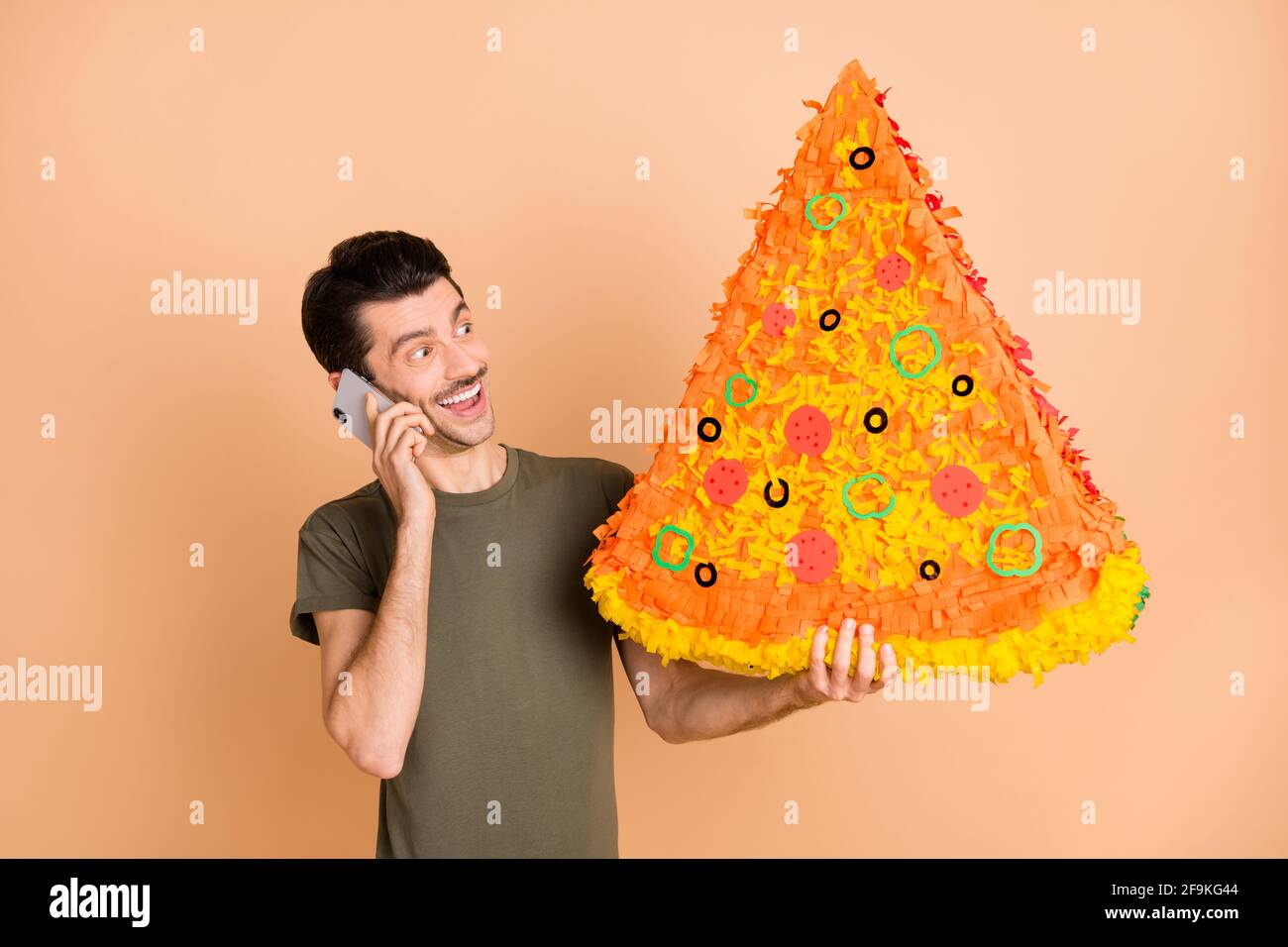 Photo of guy hold pizza pinata telephone conversation wear green t-shirt  isolated beige color background Stock Photo - Alamy