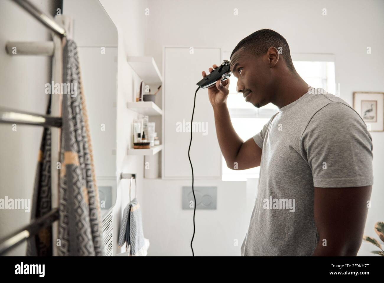 Young African man cutting his hair in his bathroom Stock Photo