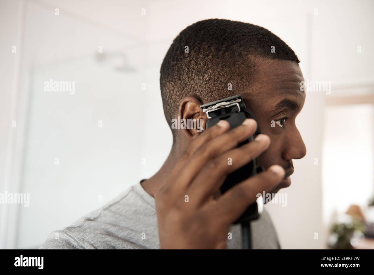 Young African man trimming his hair in his bathroom Stock Photo