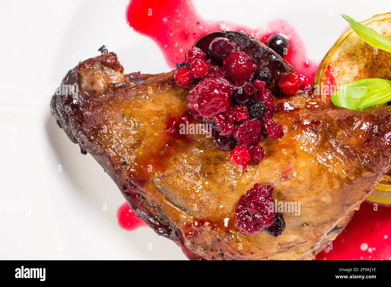 Delicious duck leg confit with red berry sauce and baked sliced apple
