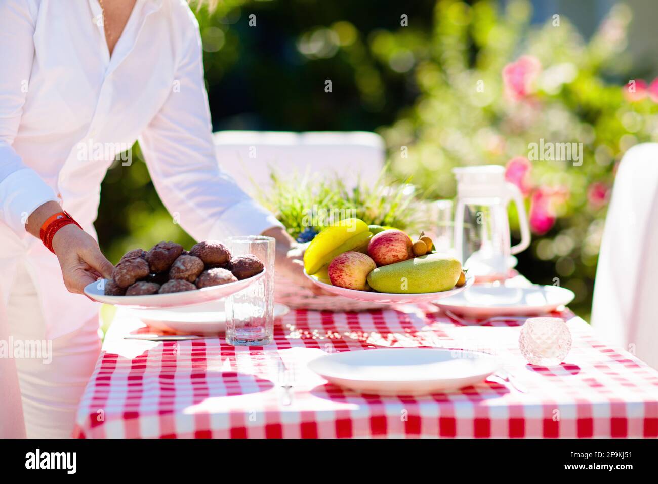 Woman setting table outdoors. Garden summer fun. BBQ in sunny backyard. Senior lady cooking lunch. Party decoration. Female with fruit outdoor. Stock Photo