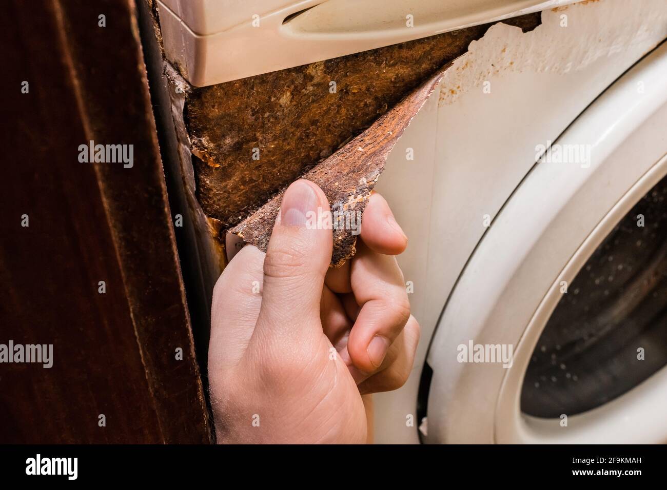 Hand holds rusty peeling layer from an old washing machine Stock Photo
