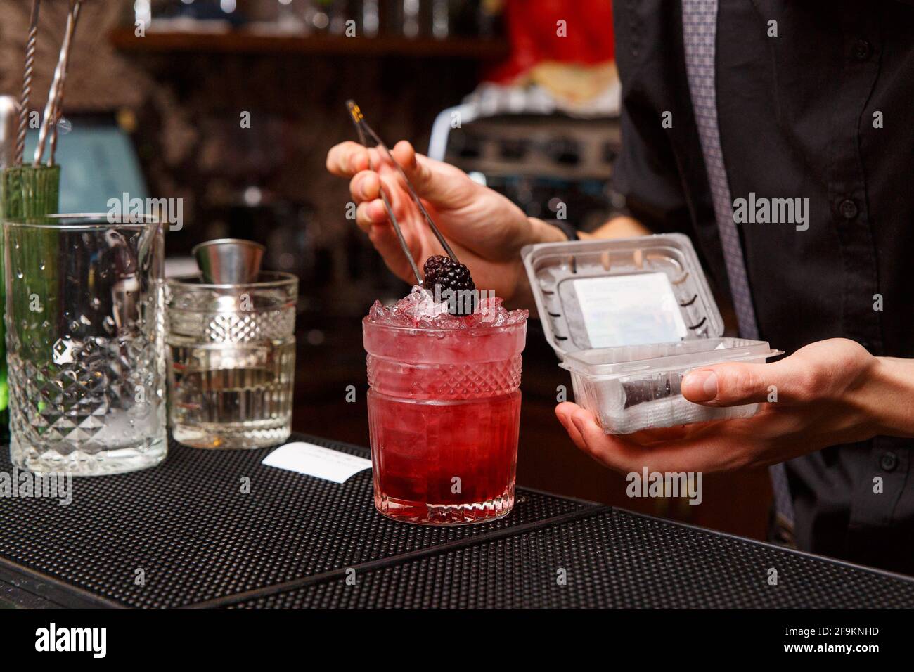A male bartender uses tweezers to carefully decorate the finished cocktail.  Bartender work concept Stock Photo - Alamy