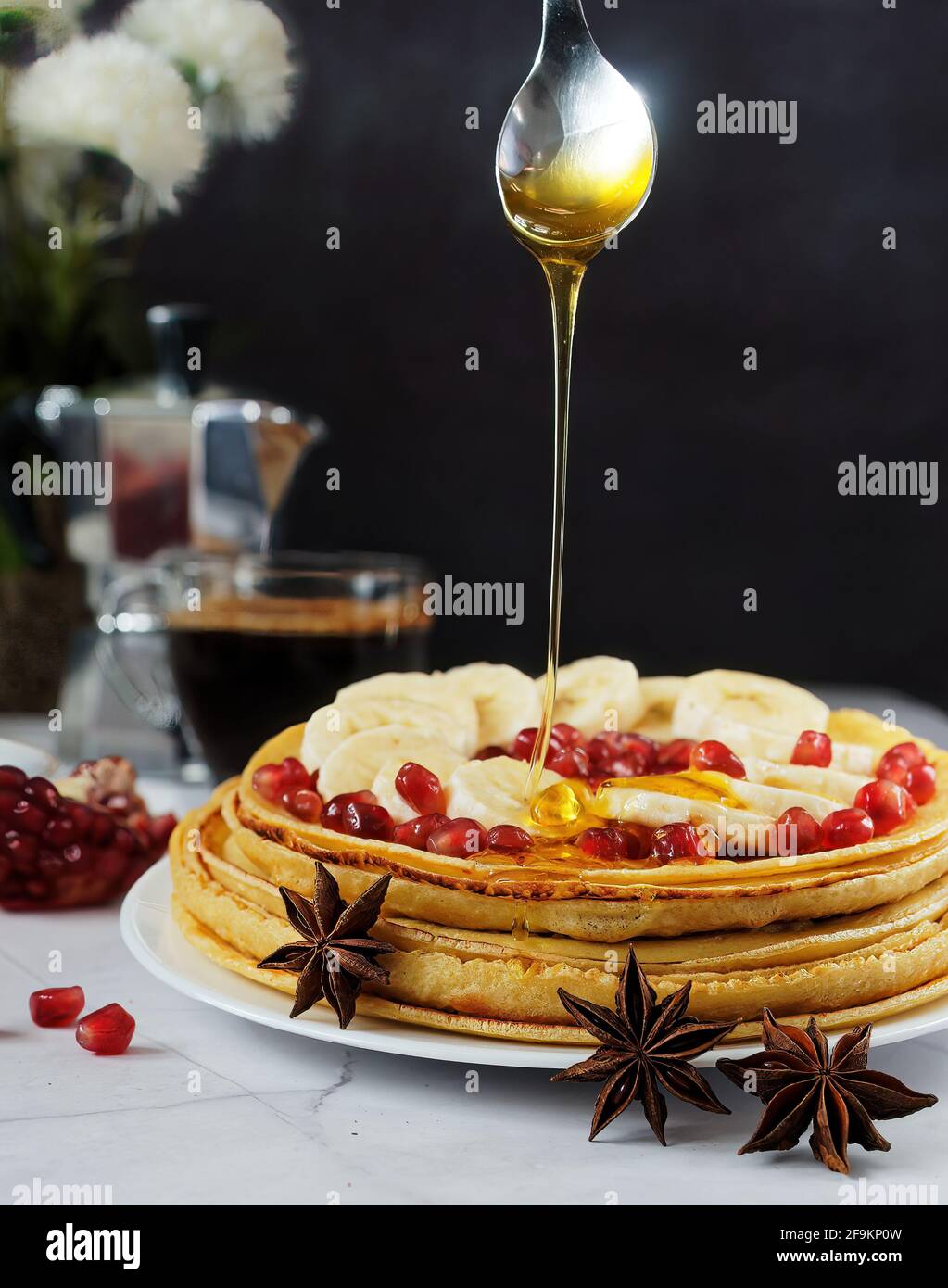 Honey pouring over stack of pancakes with banana and pomegranate Stock Photo