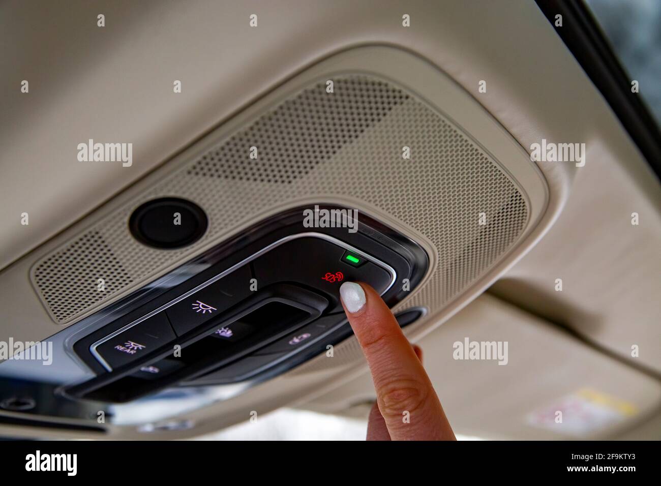 female driver's finger presses sos button on the ceiling panel of a modern car Stock Photo